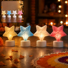 Four glowing star-shaped LED tealight candles in yellow, blue, white, and pink on a festive floor with petals.