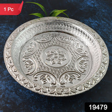 A round silver-colored plastic pooja thali with intricate embossed floral and geometric patterns, with a red 