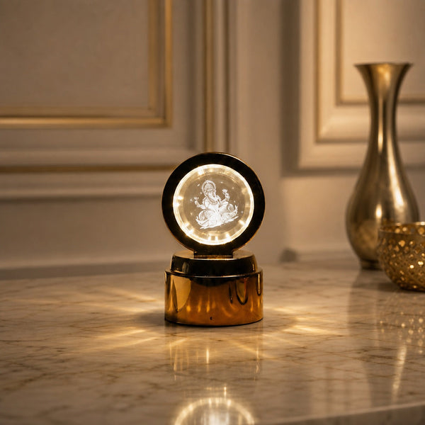 A golden base lamp with a round crystal displaying a glowing Ganesha, on a marble table with a golden vase.