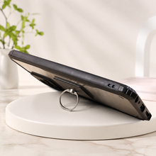 Black smartphone propped up on a white circular stand using a silver ring holder.