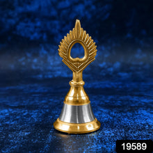 A small brass and steel pooja bell with a peacock feather design stands against a textured dark blue background.
