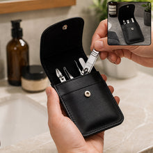 Hands holding an open black leather case with silver manicure tools inside, with a bathroom sink in the background.