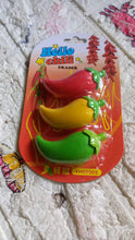 A blister pack of three chili pepper erasers in red, yellow, and green, resting on a textured, light-colored surface.