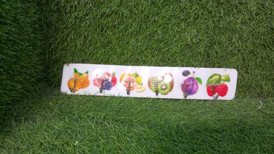 A white adhesive wall hook strip with fruit designs is placed on a vibrant green artificial grass surface.