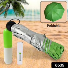 A folded green and silver umbrella with a green and white capsule case on a sandy beach.