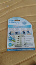 The white silicone tub drain hair catcher is shown in its retail packaging on a textured yellow surface.