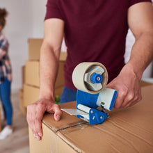 A person using a blue tape dispenser to apply transparent packing tape to a large cardboard box.