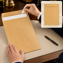 A person peeling the self-seal strip off a large brown kraft envelope on a desk.