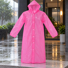 A pink translucent rain coat with a hood and white snap buttons hangs outdoors in the rain.