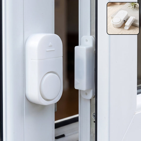 A white magnetic door and window security alarm is installed on a white window frame, with the two pieces separated.