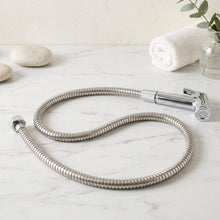 A coiled stainless steel hose with a chrome bidet sprayer lies on a white marble surface with decorative stones.