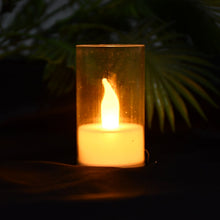 A single LED flameless candle in a transparent cover glowing brightly against a dark, blurry green background.