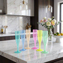 Six colorful plastic champagne flutes on a marble countertop with flowers and lemons in the background.
