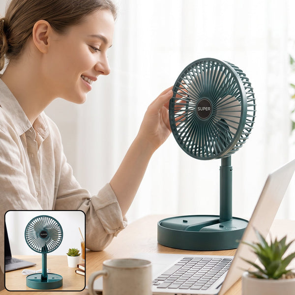 A woman adjusts a dark green portable fan on a wooden desk with a laptop and coffee mug.