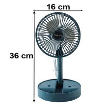 A dark green portable fan, folded flat, next to a brown cardboard box on a light wooden surface.