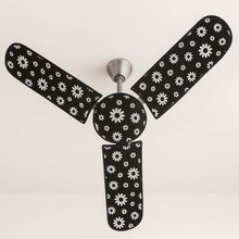 A ceiling fan with black and white floral dust covers on its blades and motor, viewed from below.