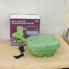 A green portable washing machine, collapsed with its lid closed, sits next to its product box and power adapter on a wooden