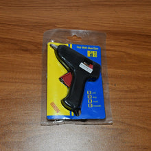 A hot melt glue gun in clear plastic packaging with yellow and blue backing, on a wooden surface.