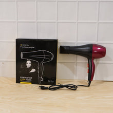 A red and black hair dryer with its black packaging box and power cord sits on a light wooden surface.