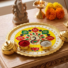 A pooja thali with a peacock design, two small bowls, a Ganesha idol, and a lit oil lamp.