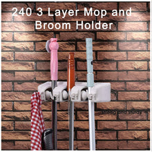 White three-slot wall-mounted mop and broom holder against a brick wall, holding a pink broom, a brown broom, and a blue