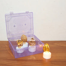 Three golden leaf LED candles are inside an open clear plastic box, with one candle outside on a wooden surface.