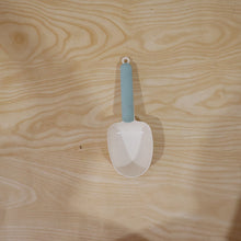 A white plastic measuring spoon demonstrating its use as a bag clip on a food bag.