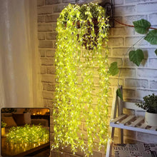 A hanging basket with long strands of green leaf string lights cascading down a brick wall, illuminated.