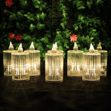 Eight clear ribbed LED flameless candles with warm glow arranged in two rows against a green leafy background.