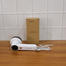 The white and dark grey lint remover, its USB cable, and its brown cardboard packaging box on a wooden surface.