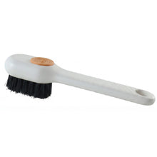 A white scrubbing brush with black bristles and an orange button is shown on a plain white background.