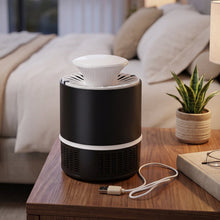 A black and white Mosquito Killer Lamp with a USB cable on a wooden nightstand with a plant and book.