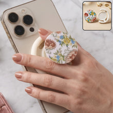 A hand holds a white smartphone with a round pop socket featuring a white background and colorful paisley floral – view 8
