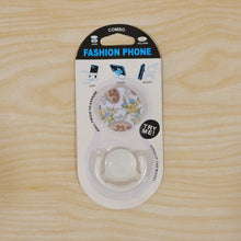 The versatile mobile phone holder with its enamel watermelon design, functioning as a kickstand on a flat surface.