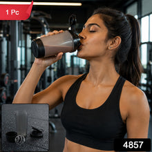 A woman in a black sports bra drinks from a grey and black shaker bottle in a gym, with a red 