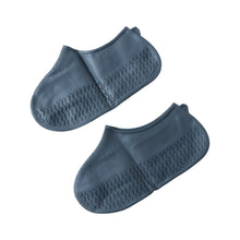 Two dark grey silicone shoe covers with textured soles are arranged on a plain white background.