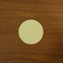 A single round beige adhesive pad centered on a warm brown wooden surface.