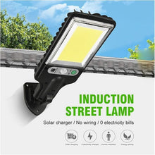 A black solar LED street light is mounted on a white wall with a tiled roof, displaying text about its solar charging and