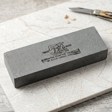 Gray rectangular sharpening stone with black text and tiger logo on a white marble surface next to a small knife.