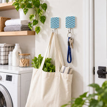 Two chevron-patterned adhesive hooks hold a canvas tote bag and a set of keys in a bright laundry room.