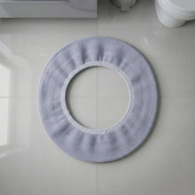 A light grey elastic toilet seat cover laid flat on light grey tiled flooring.