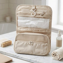 A beige hanging toiletry bag with empty clear and mesh pockets, positioned in a bathroom setting.