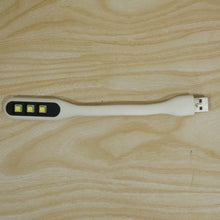 A white flexible USB LED light with three yellow LED bulbs and a USB-A connector resting on a light wood grain surface.
