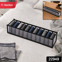 A gray 11-section fabric organizer with rolled socks on a white bedspread, with a red 