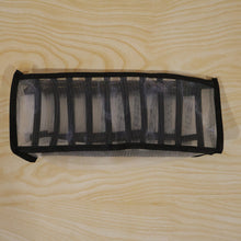 A white and black mesh fabric organizer is shown unfolded on a light wooden surface.