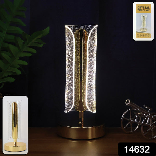 A lit gold and clear crystal table lamp on a dark wooden surface with a small cannon decoration.