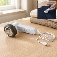 White and dark grey fabric lint remover with a USB cable on a wooden table, with an inset showing it in use on a navy