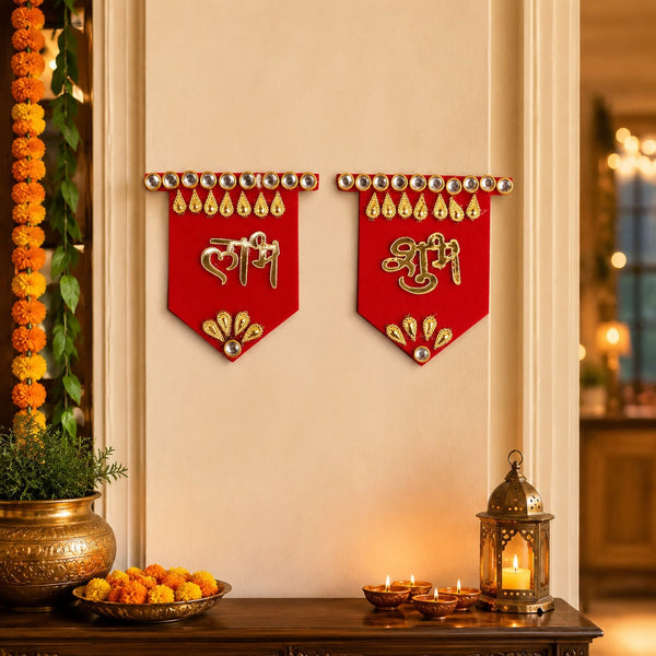 Two red Shubh Labh wall hangings with gold and clear stone embellishments, displayed on a light wall above a wooden table