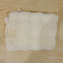 A folded cream fluffy faux fur rug swatch on a light wooden surface.