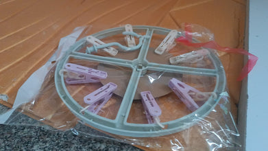 A light blue circular drying rack with purple and white clips is sealed in clear plastic packaging.